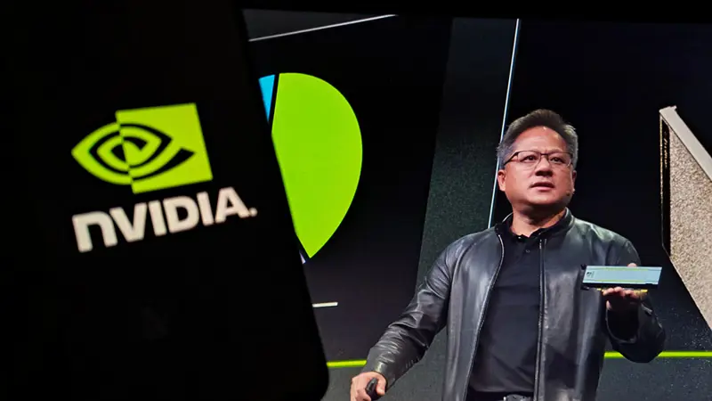 En person på en scen visar upp en datorkomponent under en presentation, med Nvidias logotyp projicerad i bakgrunden.